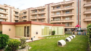 A multi-story residential building with balconies, a small garden area with a red umbrella, and a covered outdoor seating area.