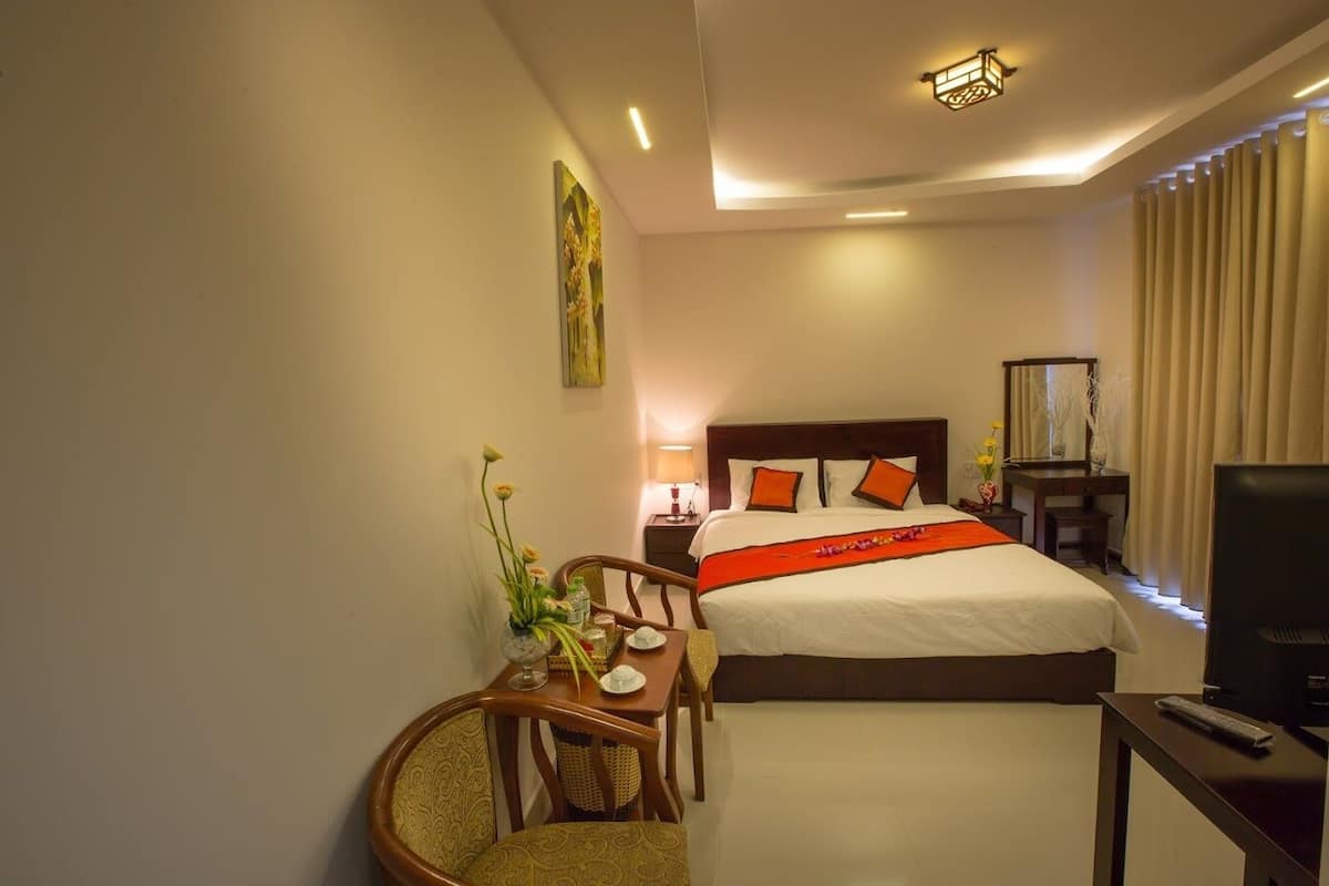 A hotel room with a large bed, a desk with a chair, a TV, and a nightstand with a lamp.