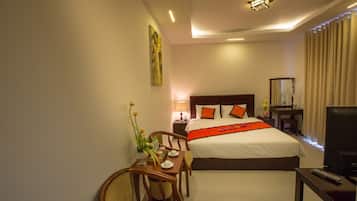 A hotel room with a large bed, a desk with a chair, a TV, and a nightstand with a lamp.