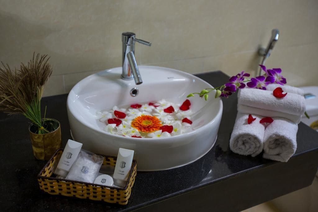 A bathroom sink with rose petals, a small vase with dried plants, and a basket of toiletries.