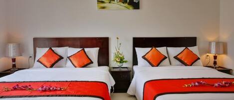 Una habitación de hotel con dos camas, cada una con ropa blanca y almohadas anaranjadas, un cuadro en la pared y un florero con flores en la mesita de noche.