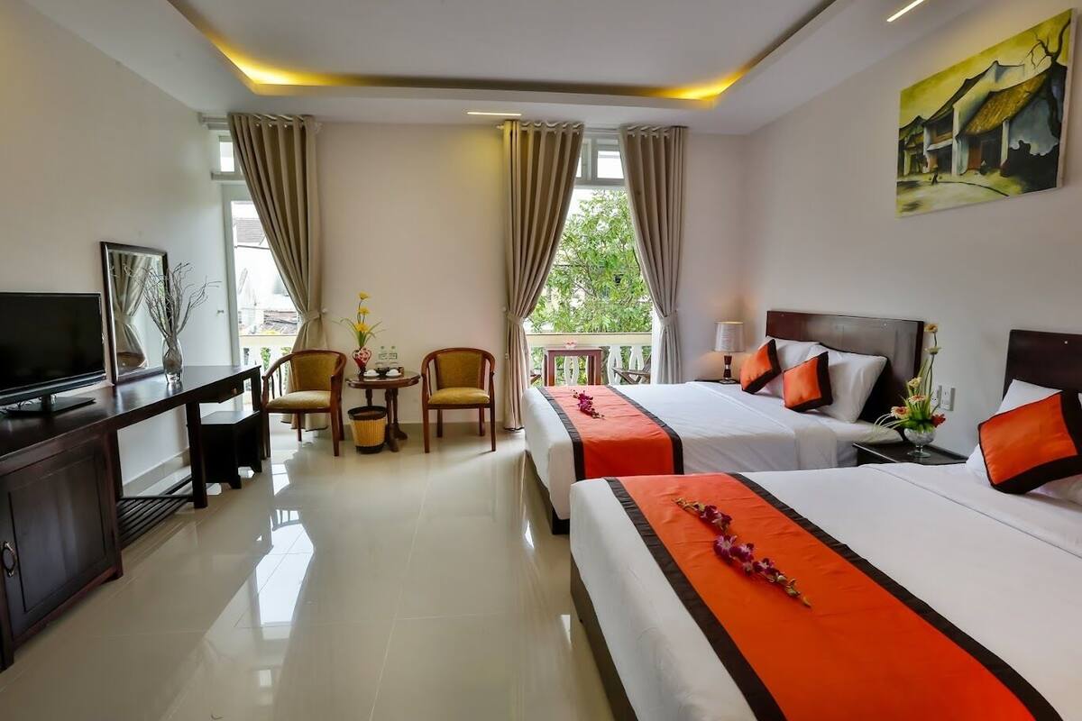 A hotel room with two beds, a TV, a desk with a chair, and a balcony with curtains.