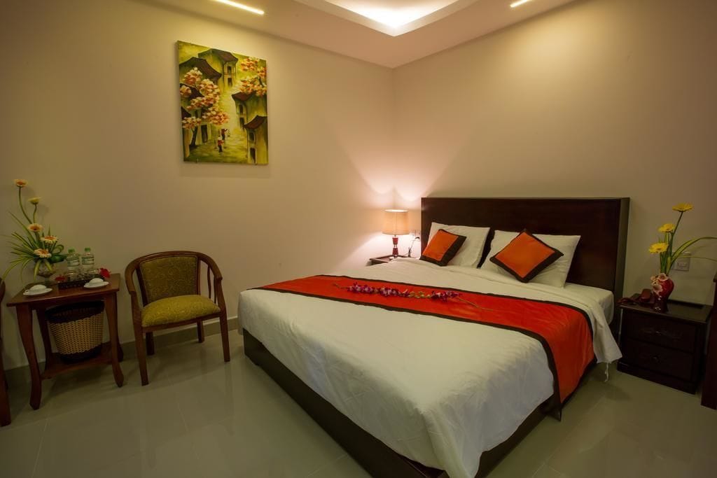 A neatly arranged bedroom with a bed, bedside table, chair, and a painting on the wall.