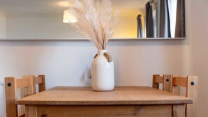 Een houten tafel met een witte vaas gevuld met veren, voor een effen muur met een spiegelbeeld.