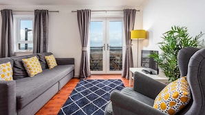 Een moderne woonkamer met een bank, fauteuil en een tv op een bijzettafeltje.