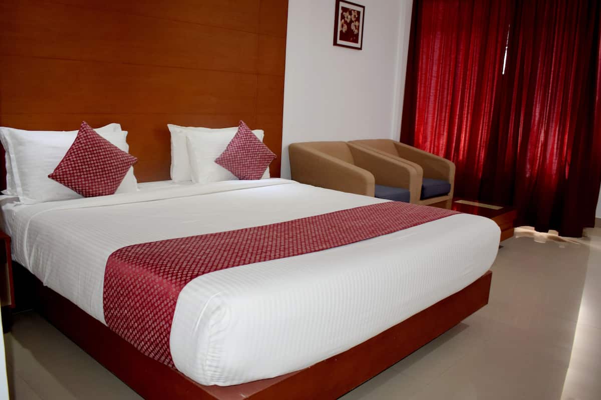 A hotel room with a large bed, two armchairs, a red curtain, and a framed picture on the wall.