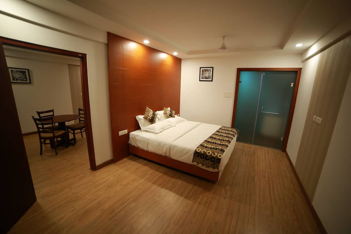 A bedroom with a wooden floor, a bed with a patterned bedspread, a desk with chairs, and a door with a frosted glass panel.