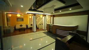A modern hotel lobby with a reception desk, seating area, and a staircase.