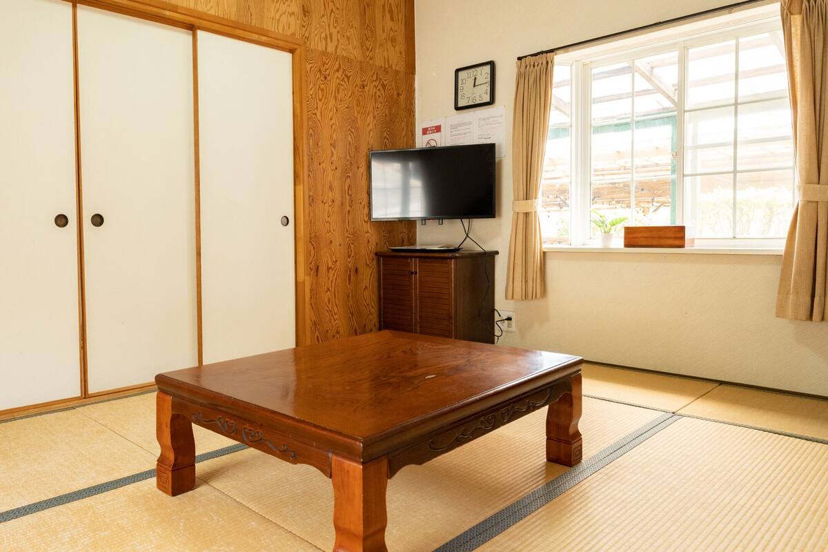 A traditional Japanese room with tatami flooring, a wooden table, a television on a stand, and sliding doors.
