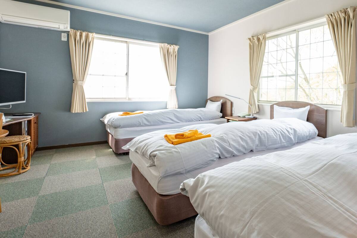 A hotel room with two beds, a television, and a window with curtains.