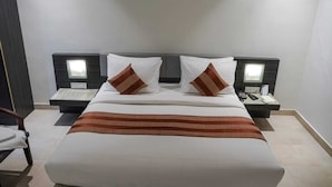 Una cama bien tendida con una colcha a rayas, dos mesitas de noche con lámparas y un tocador con un teléfono y un control remoto.