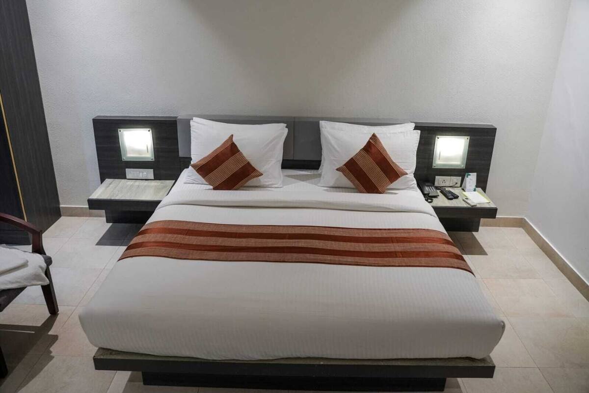 A neatly made bed with a striped blanket, two bedside tables with lamps, and a nightstand with a phone and a remote control.