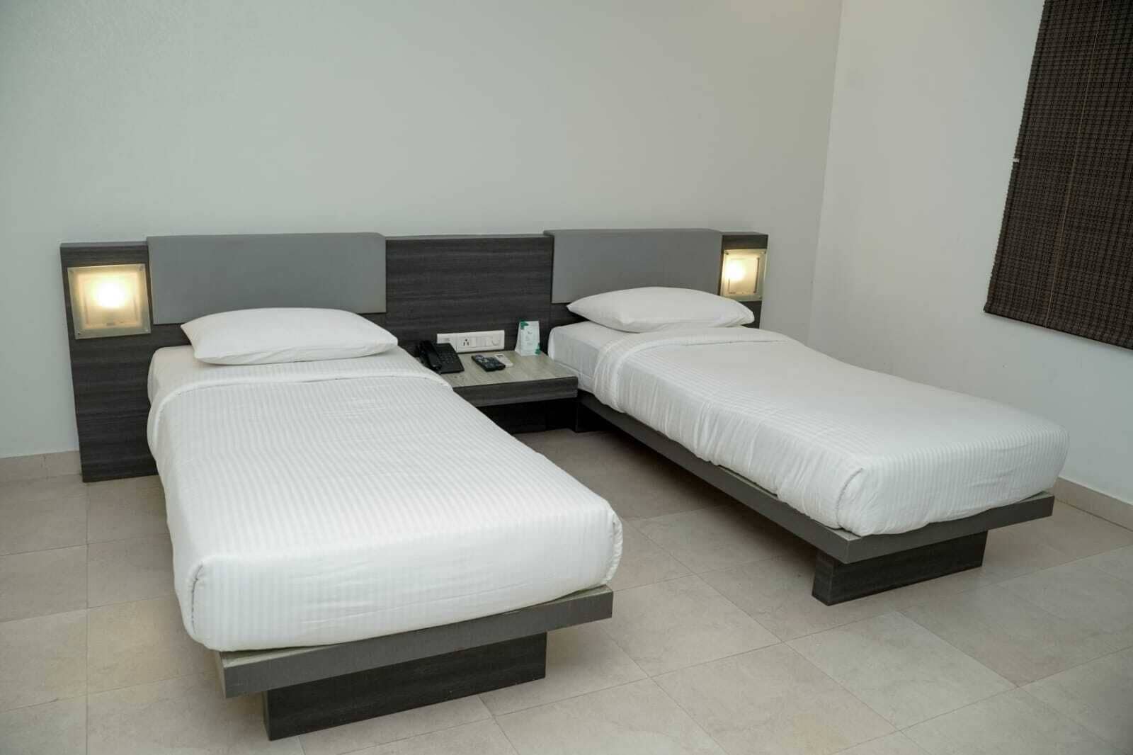 Habitación de hotel con dos camas individuales, una mesita de noche con un teléfono y una lámpara, y una lámpara de pared.