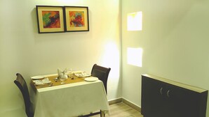 Un comedor con una mesa preparada para dos personas, sillas, un armario y dos obras de arte enmarcadas en la pared.