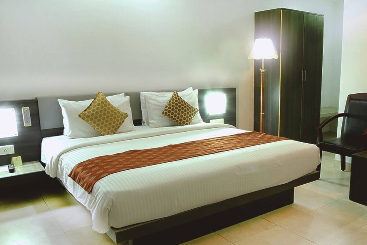 A hotel room with a large bed, bedside tables, a wardrobe, a desk with chairs, and framed artwork on the wall.