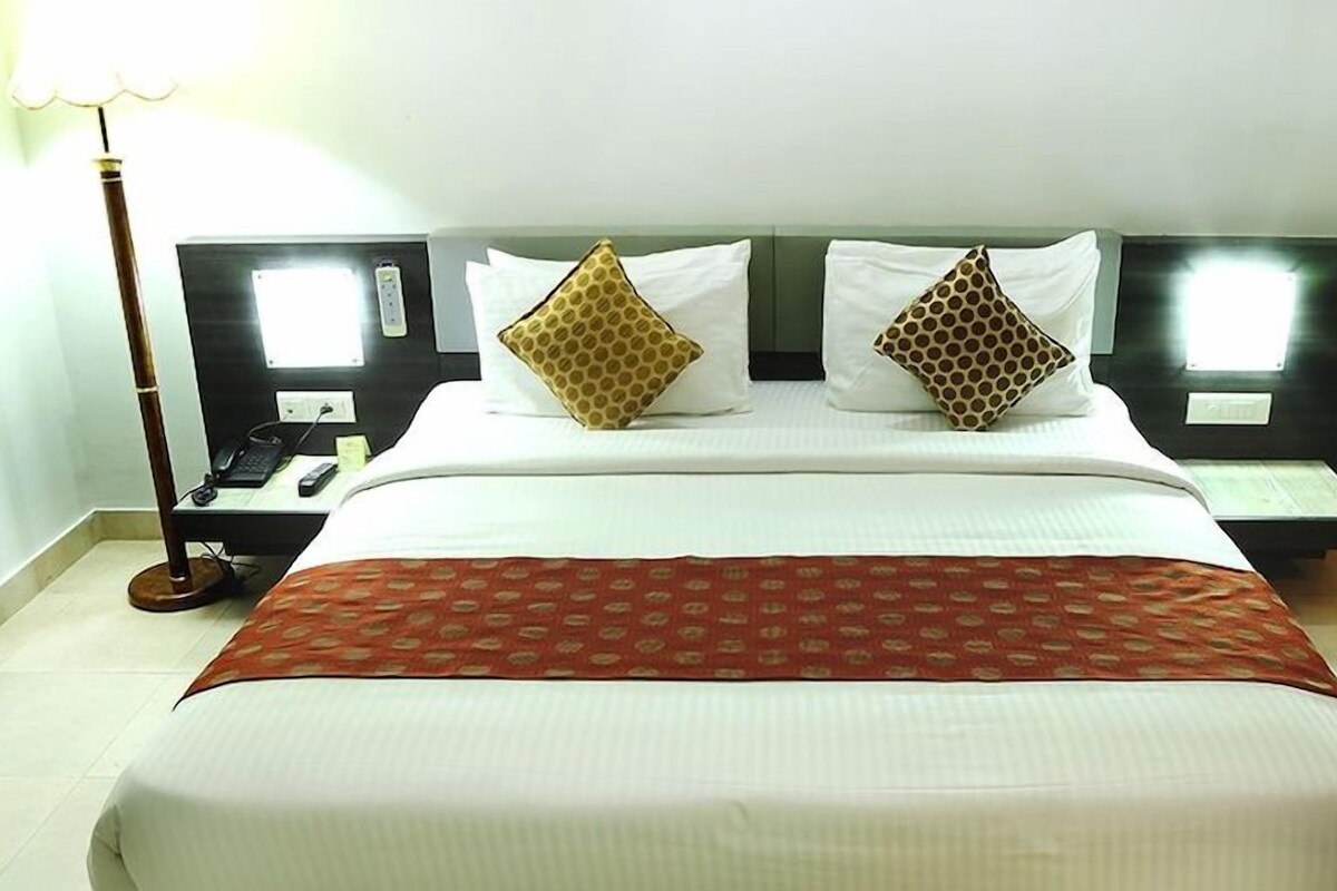 Une chambre d’hôtel avec un grand lit, deux oreillers, une table de chevet avec une lampe et une petite table de nuit avec un téléphone.