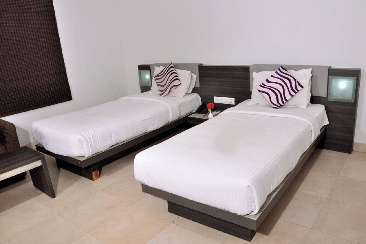 Two single beds with white linens and striped pillows, a small bedside table with a vase of flowers, and a dark wooden headboard.