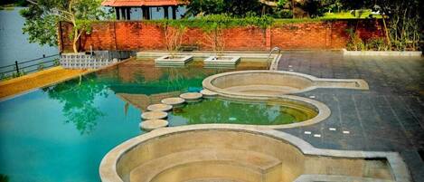 A swimming pool with a unique design, a gazebo, and a brick wall.