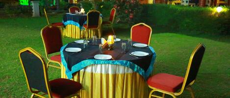 An outdoor dining area with round tables, chairs, and a tablecloth.