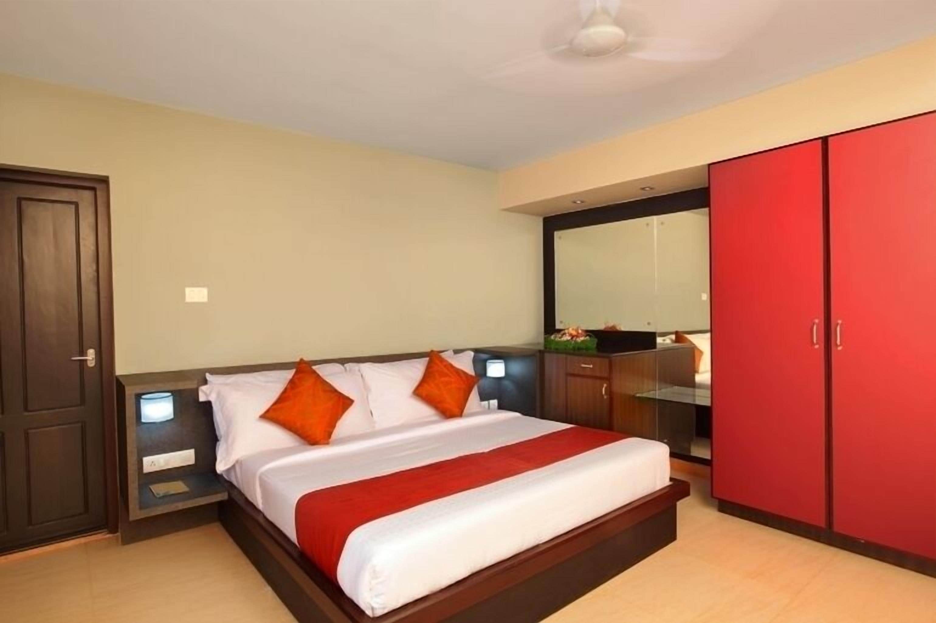 Una habitación de hotel con cama, mesitas de noche, un armario rojo y un espejo.