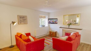 A living room with two red sofas, a floor lamp, a television, a radiator, a window with a view, and a mirror on the wall. - Corffe Cottages, Sunny Devon escape, sleeps 4, heated indoor pool (Barnstaple)