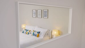 A neatly made bed with white linens and colorful pillows, two bedside lamps, and three framed artworks on the wall. - Corffe Cottages, Sunny Devon escape, sleeps 4, heated indoor pool (Barnstaple)