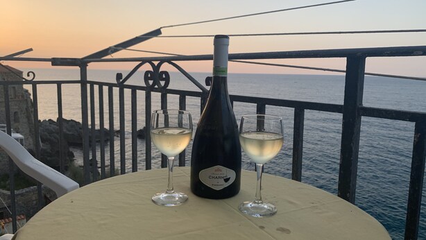 Une table avec une bouteille de vin et deux verres sur un balcon donnant sur la mer.
