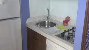 Une cuisine de taille réduite, équipée d’un réfrigérateur, d’un évier, d’une cuisinière et de placards.