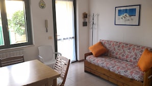 A room with a wooden dining table, a sofa with orange cushions, a chair, a door with a curtain, a wall-mounted telephone, and a framed picture. - Holiday house in residence near the sea (Borgo Hermada 29)