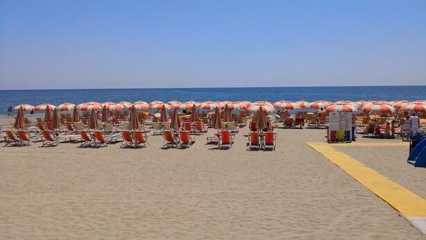 A beach with rows of orange and white striped umbrellas and beach chairs. - Holiday house in residence near the sea (Borgo Hermada 29)