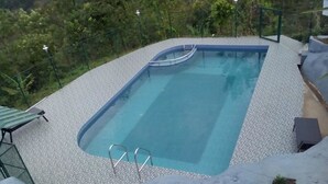 Une piscine rectangulaire à l’eau d’un bleu limpide, entourée d’une terrasse bordée de galets.