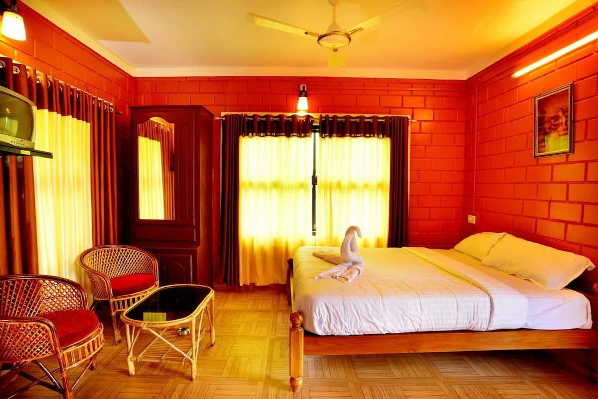 A hotel room with a bed, two wicker chairs, a small table, a television, and a mirror.