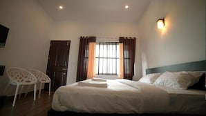 Une chambre à coucher comprenant un lit, deux chaises, une fenêtre avec des rideaux et un luminaire fixé au mur.