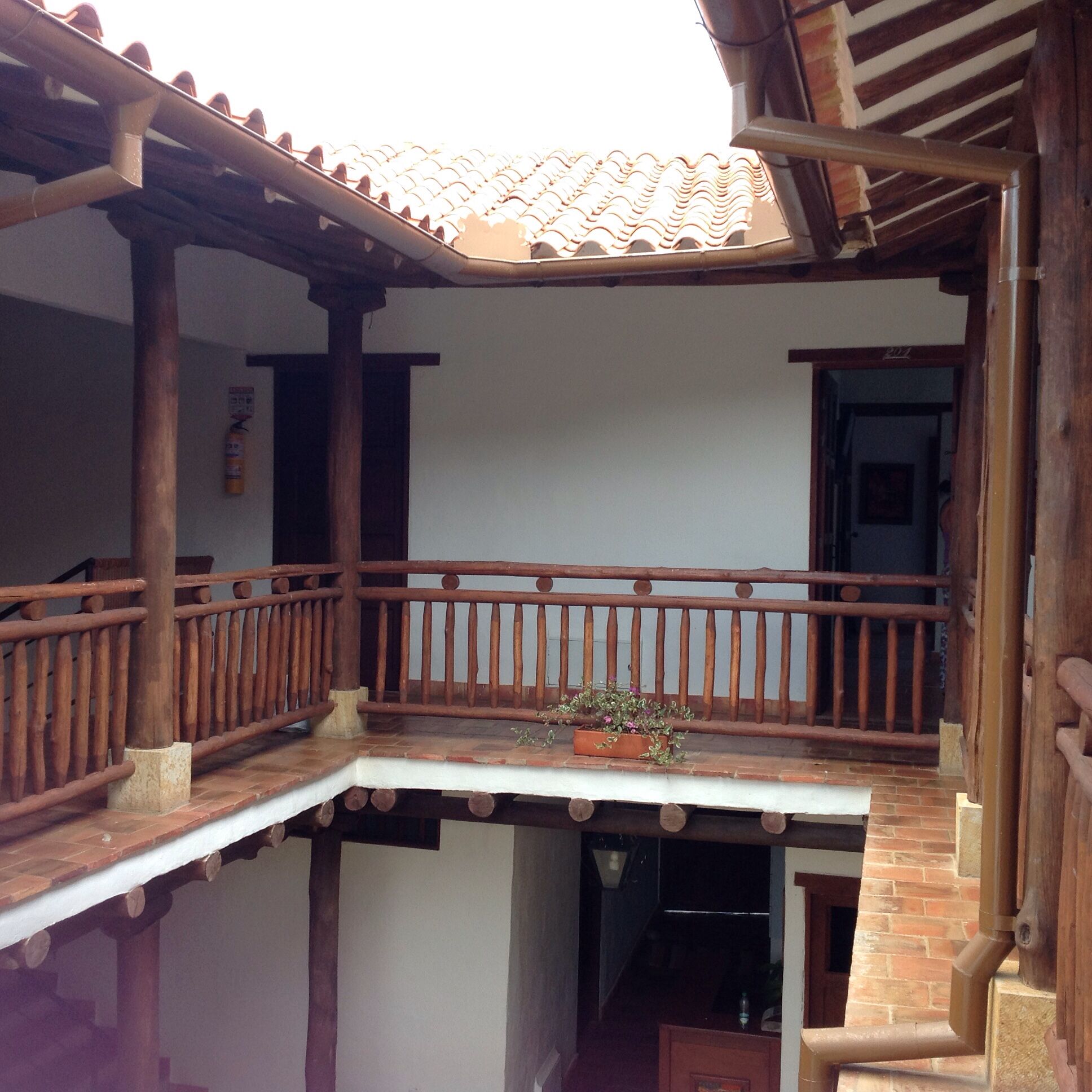Un balcon en bois avec un toit recouvert de tuiles, une balustrade en bois et un pot de fleurs.