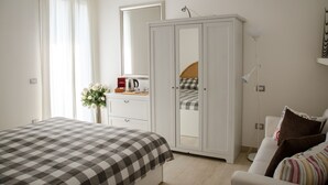 Ein Schlafzimmer mit Bett, Kleiderschrank, Nachttisch, Lampe und einem Fenster mit Vorhängen.