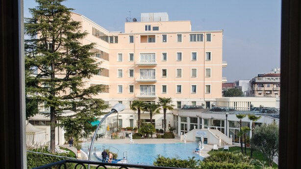 Ein Hotel mit Schwimmbad, ein Gebäude mit mehreren Balkonen und ein gepflegter Gartenbereich.