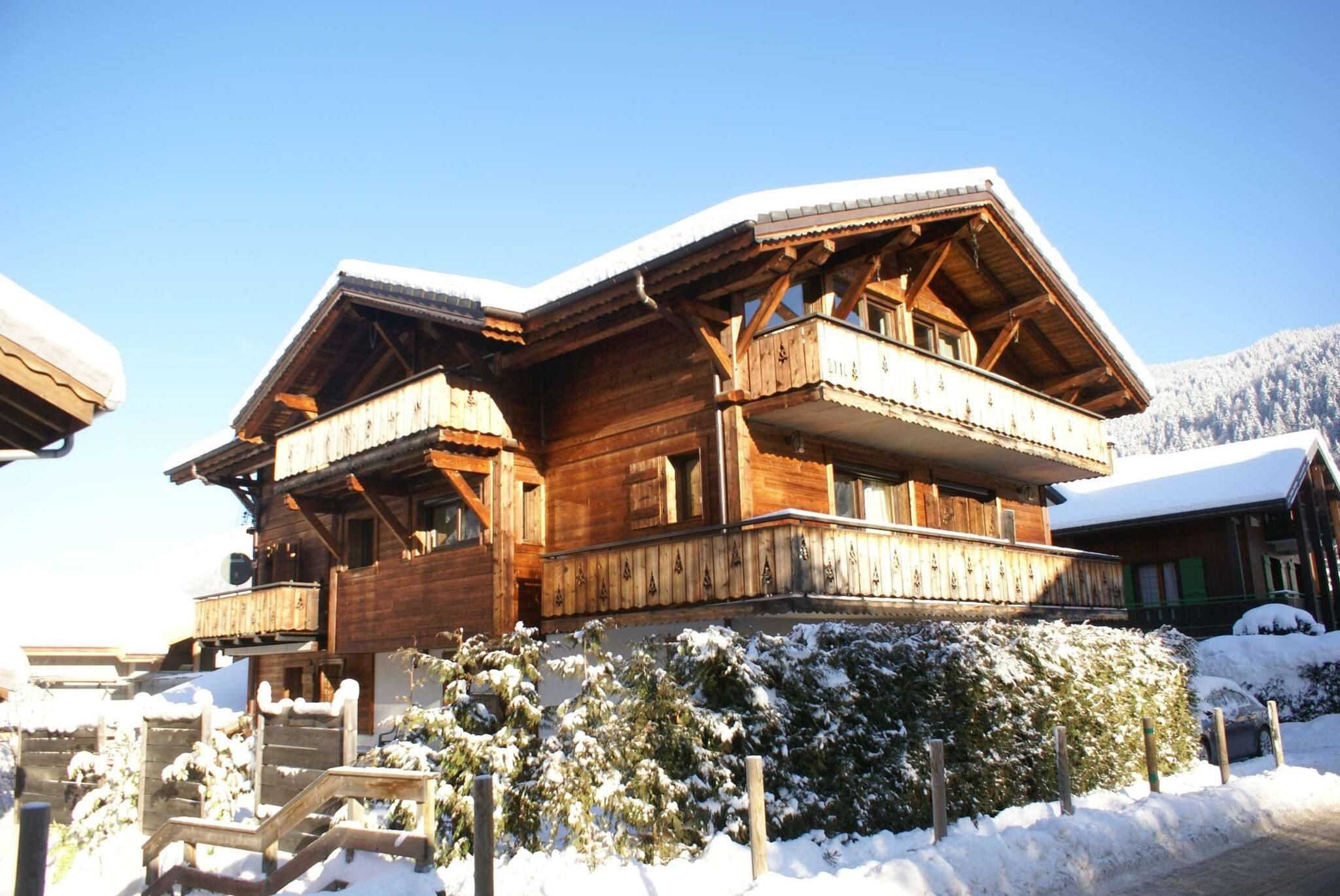 A wooden chalet with balconies, surrounded by snow-covered trees and a clear sky.