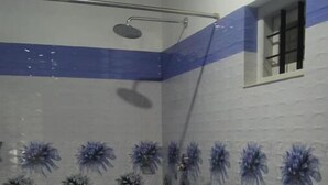 A bathroom with blue and white tiles, a shower, a bucket, and a small window. - Green Island Resort (Vaikom)
