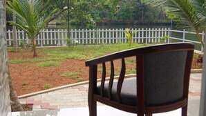 A chair in a covered outdoor area with a view of a white picket fence and greenery. - Green Island Resort (Vaikom)