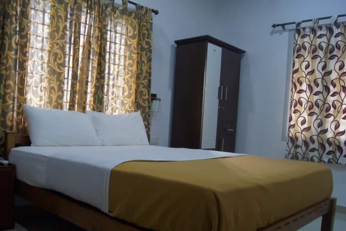 A single bed with a white and yellow bedspread, a wooden nightstand with a telephone, and a wardrobe with a mirror.
