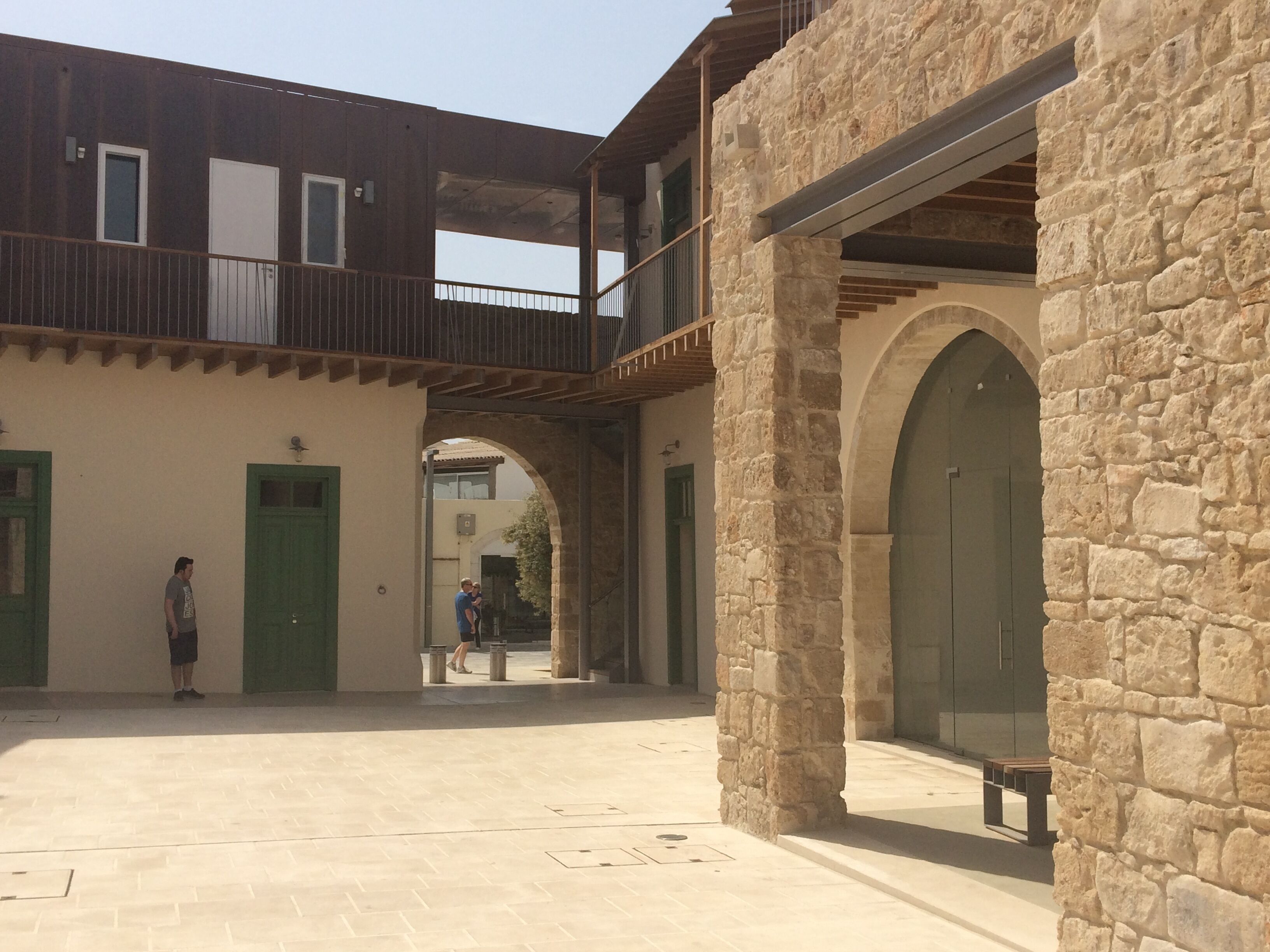 A courtyard with a stone building, a wooden balcony, and a green door.