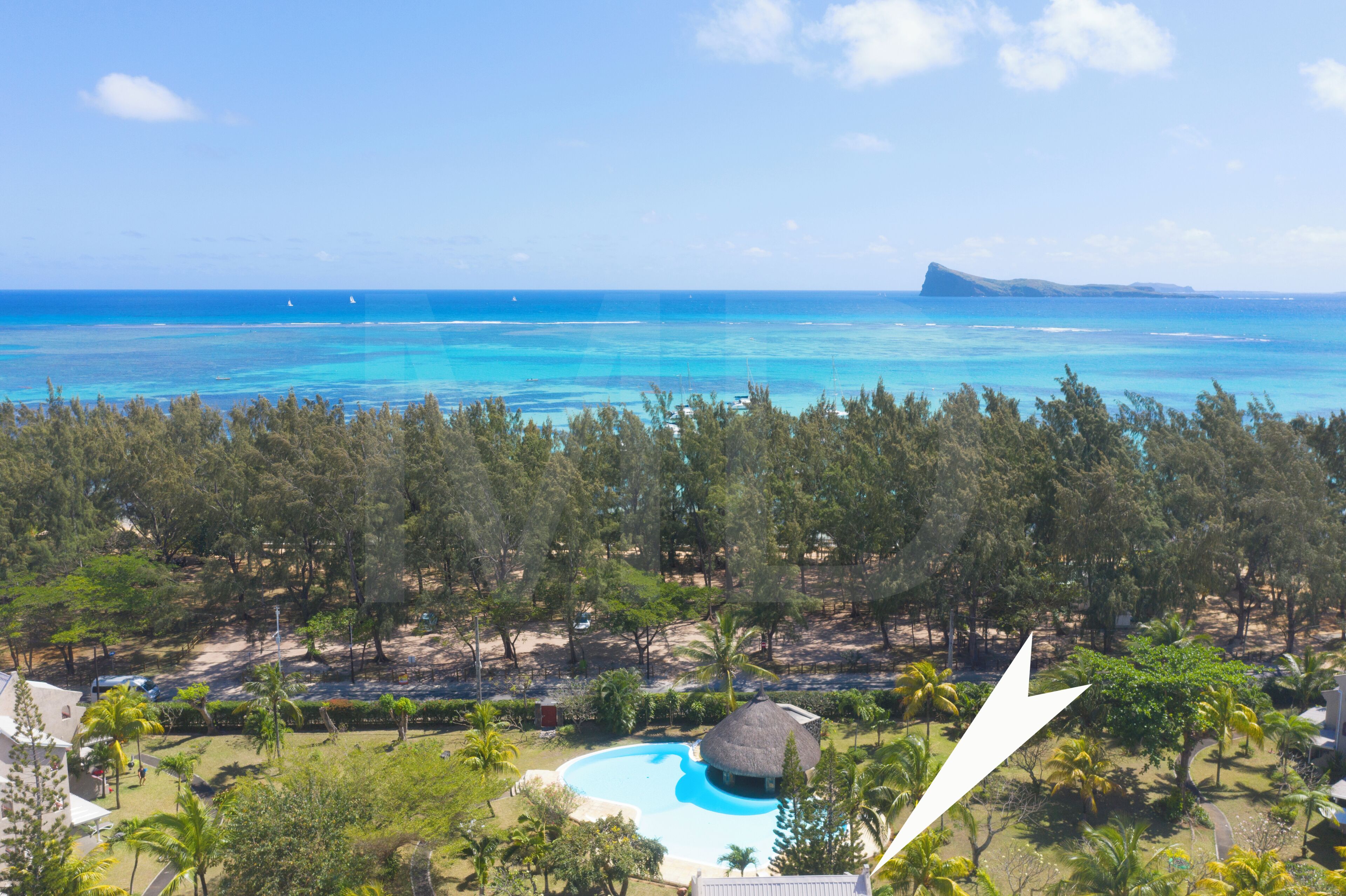 Ein tropisches Resort mit Schwimmbad, üppiger Vegetation und Blick auf den Ozean.