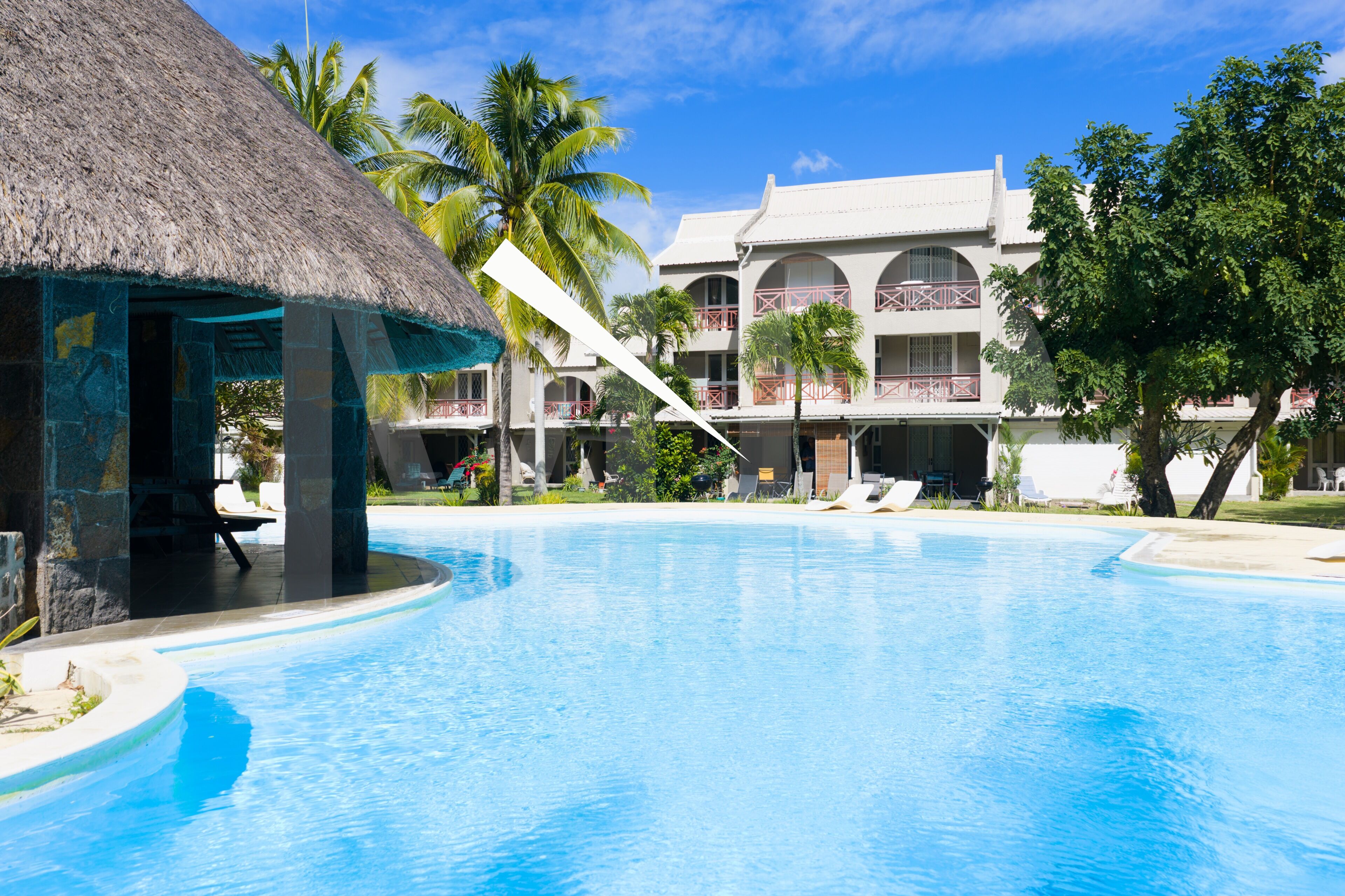 Un resort con piscina, edificios de techo de paja y construcciones de varios pisos con balcones.