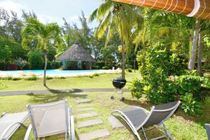 A poolside area with lounge chairs, a barbecue grill, and a thatched-roof hut.