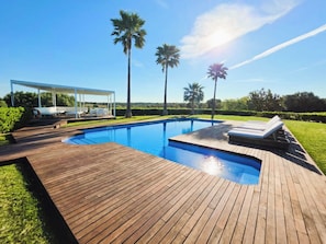Une piscine avec une terrasse en bois, des chaises longues et un espace salon abrité.
