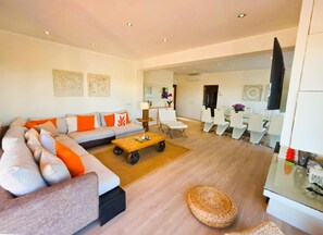 A modern living room with a sectional sofa, a coffee table, and a dining area with white chairs.