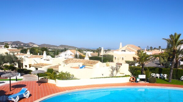 A pool area with lounge chairs, a lifebuoy, and a view of a residential area with houses and hills in the background.