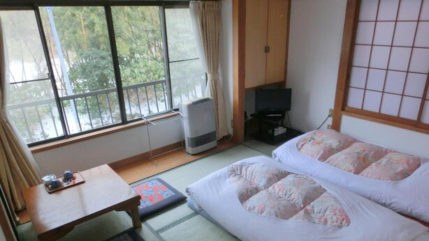 A traditional Japanese room with tatami flooring, a futon bed, a small table with a tray, a heater, and a TV. - Moto-Hakone Guest House (Hakone)