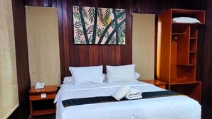 A hotel room with a wooden bed, white bedding, a bedside table with a phone, a wall-mounted painting, and a wooden wardrobe. - Exotic Komodo Hotel (Labuan Bajo)