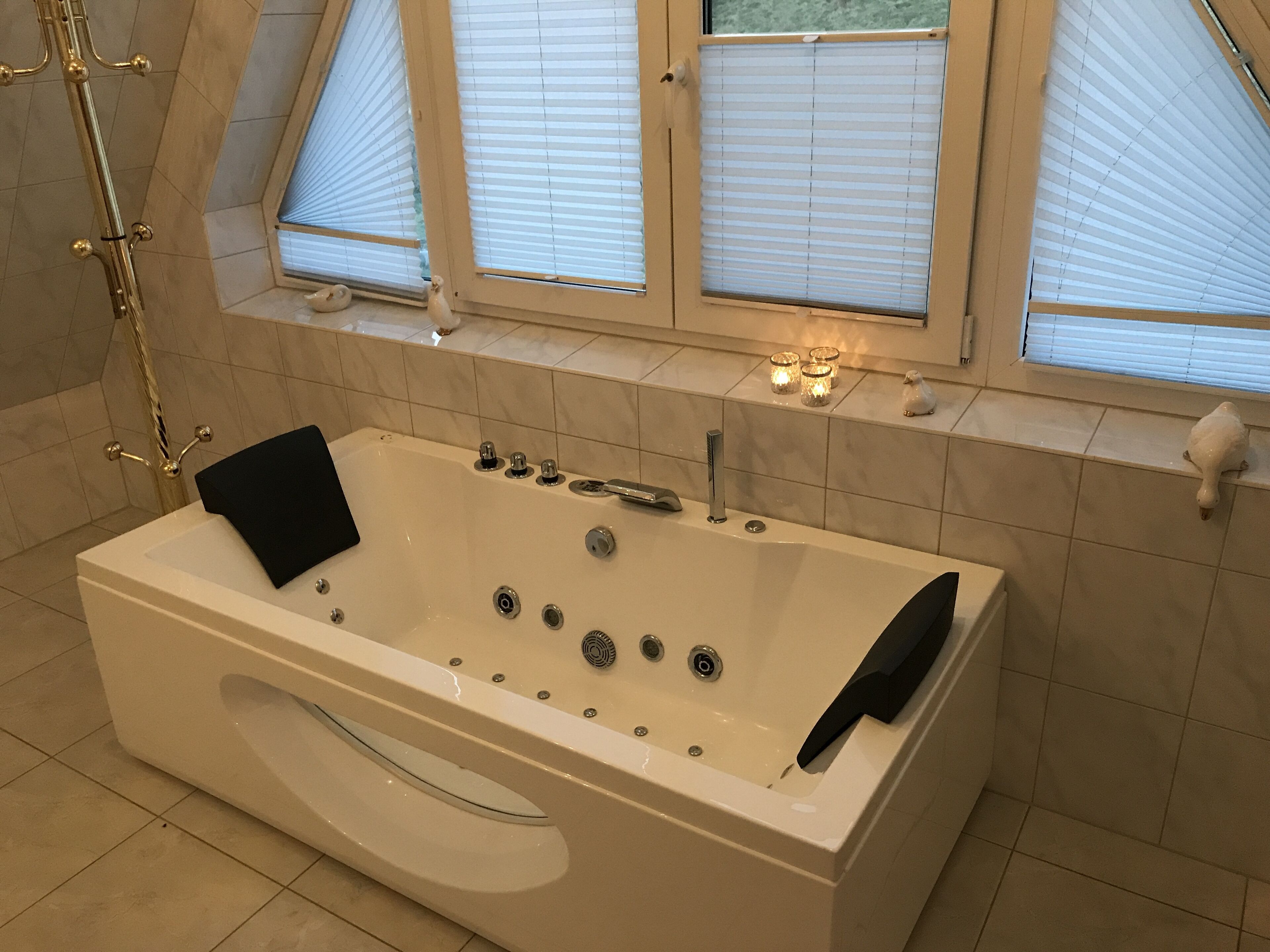 Et moderne badeværelse med et stort badekar, en glasafskærmet brusekabine og et vindue med skodder.